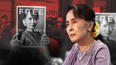 ကင်မရာရဲ့ အဝေးဘက် တစ်ဖက်ခြမ်းကို ငေးကြည့်နေတဲ့ ဒေါ်အောင်ဆန်းစုကြည်၊သူ့နောက်မှာ သူ့ကိုလွှတ်ပေးဖို့တောင်းဆိုနေတဲ့လူတွေက ဆိုင်းဘုတ်ကိုင်ထားတဲ့ အနီရောင် အဖြူရောင် အနက်ရောင် ပေါင်းစပ်ဓာတ်ပုံဖြစ်ပါတယ်၊​