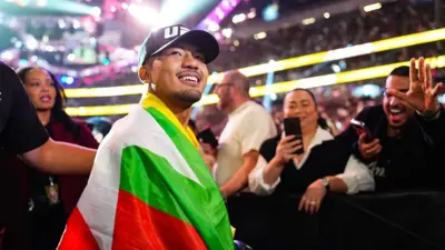 ၂၀၂၅ ခုနှစ်၊ ဒီဇင်ဘာ ၆ ရက်တုန်းက အမေရိကန်ပြည်ထောင်စု နဗားဒါးပြည်နယ်မှာ ကျင်းပတဲ့ ပြိုင်ပွဲအပြီးမှာ အဖြူ အစိမ်း အနီ အဝါရောင် မြန်မာအလံကိုခြုံ UFC တံဆိပ်ပါတဲ့ဦးထုပ်ကို ဆောင်းပြီး ပရိသတ်ဘက်ကို ပြုံးပြနေတဲ့ ဂျော့ရှူဝါ ဗန်၊ သူနောက်မှာ ပရိသတ်တွေက ဖုန်းရဲ့ ရိုက်ပြီး အားပေးနှုတ်ဆက်နေ 