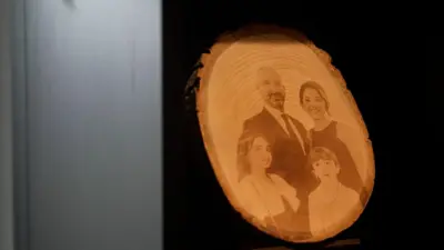 Tüzgiray ailesinin fotoğrafının yer aldığı ahşap bir işleme. Baba Tüzgiray'ın üzerinde takım elbise, anne Tüzgiray'ın üzerinde elbise var. Çocuklar da benzer şekilde şık giyinmiş.