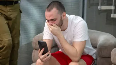 Andrey Kozlov sits crying covering his mouth whilst looking at a phone