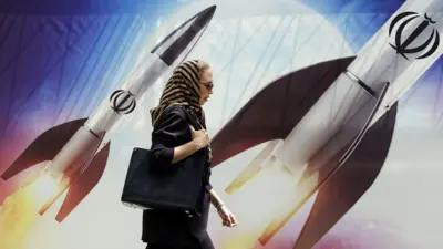 Seorang perempuan berjalan melintasi spanduk bergambar rudal Iran di Teheran, Selasa (16/04).