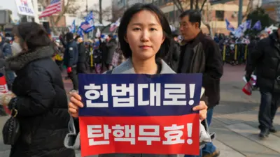 A woman holds up a sign in Korean that says President Yoon's impeachment is invalid