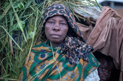 Umugore uri imbere y'akazi gasakaje ishashi n'ibiti inyuma ye hari umwana urimwo kureba ufata isanamu