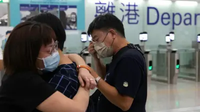 在香港機場的離港閘前,兩人相擁,另外一人以紙巾抹眼淚。