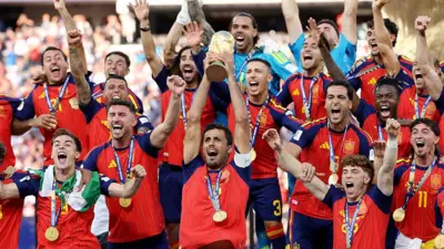 赤と紺のジャージに金メダルを下げ、腕を突き上げるなどして優勝を祝うスペイン代表。主将ロドリが優勝トロフィーを両手で持ち、高く掲げている