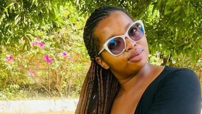 Naomi Kuria in a black top and brown shorts, sitting in a compound with green grass