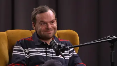 Фізик Михайло Висоцький сидить у жовтому мʼякому кріслі перед мікрофоном і усміхається. 