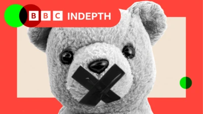 A stylised black-and-white image of a teddy bear with a bold black X over its mouth. Only the upper half of the bear is visible, set against a light peach background. The image is framed by a vibrant red border, with two small green circles added for contrast—one in the top left corner and the other in the bottom right corner.