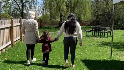 Aracely and her two daughters link hands in a park - we only see them from their back