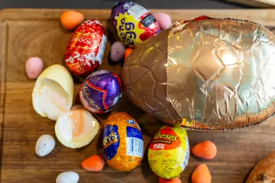 Nadziewane jajka leżą obok mini jajek oraz częściowo odwiniętego dużego jajka wielkanocnego ułożonego na drewnianej desce.