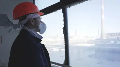 Hombre con ropa de protección mira por una ventana donde se ve la planta nuclear de Chernobyl