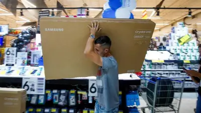 Un hombre carga la caja de un televisior de gran tamaño y marca Samsung