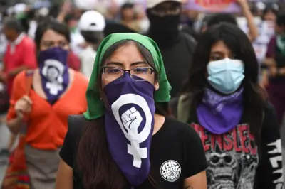 Peru'nun Lima kentinde düzenlenen bir protestoda, yeşil başörtüsü ve ağzını kapatan mavi bir eşarp takan bir kadın, diğer kadınlarla birlikte görülüyor.