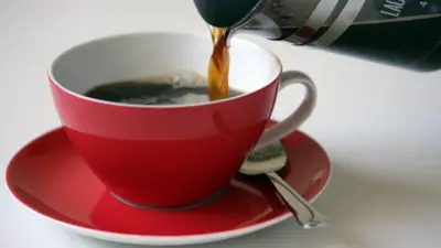 Кофе наливается в красную чашку.