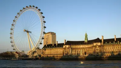 The London Eye in front of the former County Hall on the river Thames at sunset.