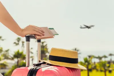 Mulher com mala cor-de-rosa e passaporte com cartão de embarque, virada para o mar com palmeiras