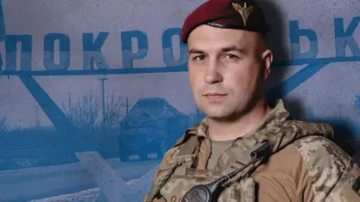 Євген Ласійчук у формі десантника, на фоні стели з написом Покровськ 