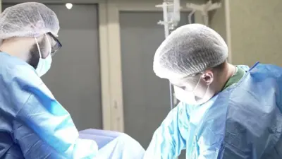 На фото крупним планом двоє хірургів у синьому спецодязі схилилися під час проведення операції військовому. 