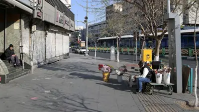 خیابان انقلاب تهران مغازه ها بسته است. یک گلفروش کنار خیابان نشسته ولی مشتری ندارد. یک نفر هم روی پله های یک شرکت نشسته. خیابان تقریبا خالی است. ساکنان میدان انقلاب، یکی از شناخته‌شده‌ترین نقاط تهران، ایران، در تاریخ سه شنبه ۲۶ اسفند ۱۴۰۴ به زندگی روزمره خود ادامه می‌دهند، پس از آن‌که ایالات متحده و اسرائیل درشنبه ۹ اسفند ۱۴۰۴ حملات گسترده‌ای علیه اهداف مختلف در ایران انجام دادند که به کشته شدن آیت‌الله علی خامنه‌ای، رهبر عالی ایران و آسیب به ساختمان‌ها و خودروهای بسیاری انجامید.