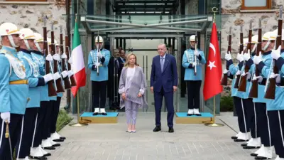 Meloni ve Erdoğan ayakta, iki yanda tören askerleri  ve iki ülke bayraklarıyla