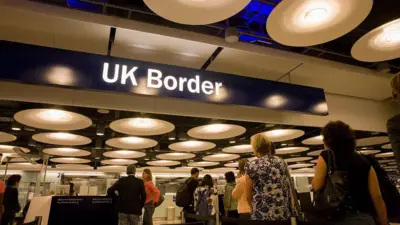 UK airport passport control. There is a blue overhead sign with UK border written on it in white. People are queuing to get their passports checked.