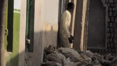 A man standing in front of a home with several bags in front of the house