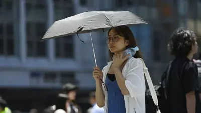 2025年6月17日に東京で、日傘を差し、水のペットボトルを首にあてながら歩く女性