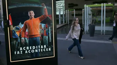 Propaganda de site de apostas em painel em rua de São Paulo, com transeunte passando ao fundo