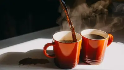 Café sendo servido em duas xícaras em uma mesa manchada de café