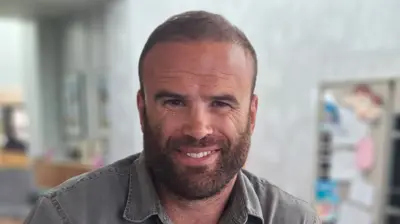 Former rugby player Jamie Roberts, with short cropped brown hair and a beard, wearing a grey shirt, smiles at the camera