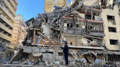 رجل يرتدي ملابس داكنة يقف أمام مبنى متضرر بشدة في العاصمة اللبنانية بيروت، عقب غارة جوية إسرائيلية أُفيد بوقوعها في 5 مارس/آذار 2026.