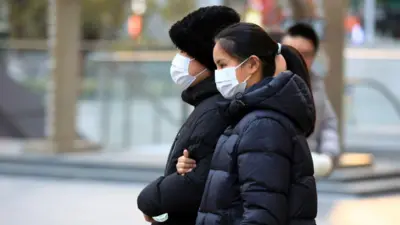 Orang-orang yang memakai masker berjalan di jalan di tengah lonjakan penyakit pernafasan.