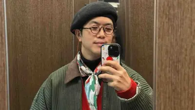 A man in a black beret and colourful scarf taking a photo in the mirror with his iPhone