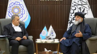 وزیر تجارت حکومت طالبان سمت راست که لنگی سیاه، پیراهن نیلی و واسکت سرمه‌ای دارد و سمت چپ، معیین وزارت نفت ایران که دریشی سرمه‌ای و پیراهن سفید دارد.