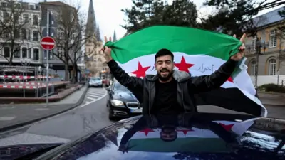 A man holds a Syrian flag in a car in Germany as he celebrates the downfall of Bashar al-Assad in his home country