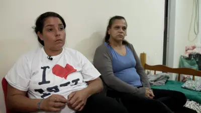 Pamela e Michele sentadasapostar vencedor da copacama, observando algo na frente delas com olhar sério