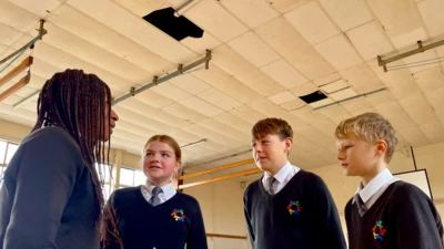 Four students stand in the gym at Patchway Community School in Bristol. Above them, two ceiling panels are missing and cracks have appeared in others