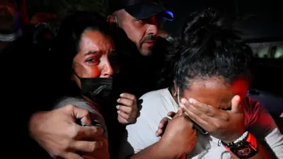 Dos mujeres lloran agarradas de la mano en medio de las operaciones de rescate tras el doble terremoto en Venezuela mientras un hombre las abraza por detrás
