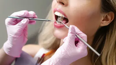 一位戴著粉紅色手套的牙醫正在用器械檢查一位女士口腔