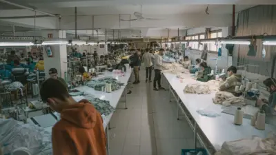 MAsalarda tekstil ürünleri var. Genç erkekler dikiş makinelerinin başında