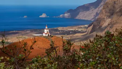 Faro rojo en medio de una isla verde y volcánica. 