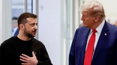 Zelensky puts his hand on his chest as he speaks to Trump, stood next to him.