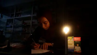 Seorang perempuan penjaga apotek menulis daftar obat dalam gelap di Aceh.