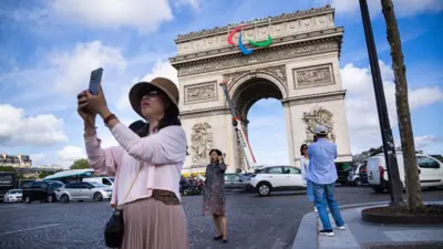 Tourists take pictures in front of the Arc de Triomphe in Paris