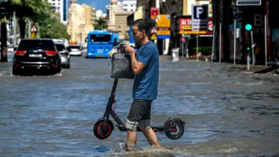 مردی اسکوتر برقی را از میان سیلاب حمل می‌کند