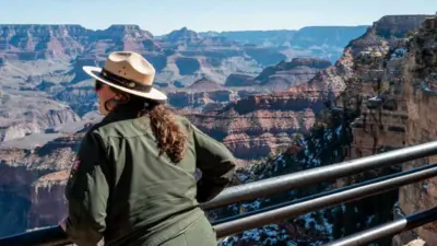 A national park ranger with a green jacket and a hat looks out into the snowy Grand Canyon National Park