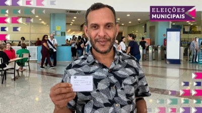 Um homem, Diogo Viroli, segura seu título de eleitor enquanto posa para o retrato em frente a um local de votação em São Paulo