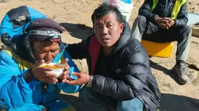 Dawa Sherpa vestindo uma jaqueta azul bebe de uma tigela oferecida por outro homem em roupas de frio