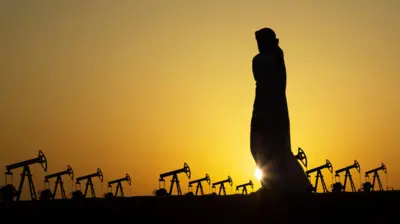 La silueta de un hombre árabe observa decenas de unidades de bombeo de petróleo contra la puesta del Sol