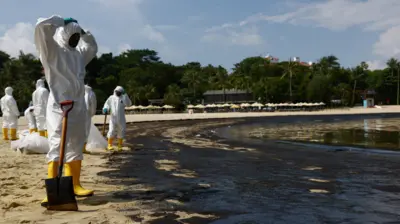 Para Pekerja yang menggunakan baju pelindung membersihkan tumpahan minyak di objek wisata Pantai Tanjong, Minggu.